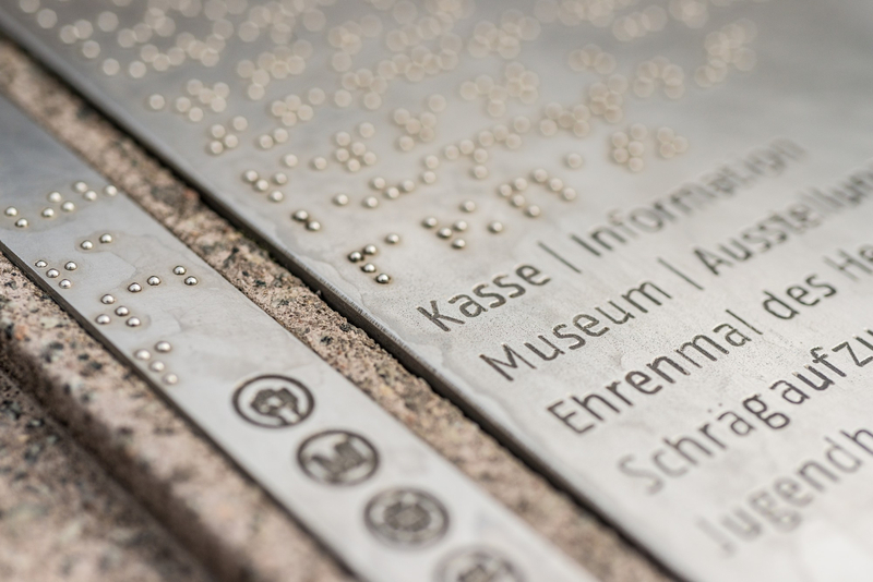Schild mit Beschriftung in Braille und Normalschrift: Kasse, Museum, Ehrenmal, Schrägaufzug