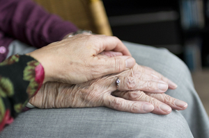 Die Hand einer Frau mittleren Alters berührt die Hände einer sehr alten Frau