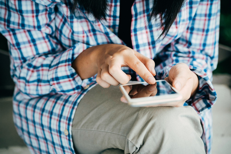 Frau mit kariertem Hemd berührt mit einem Finger das Display eines Smartphones